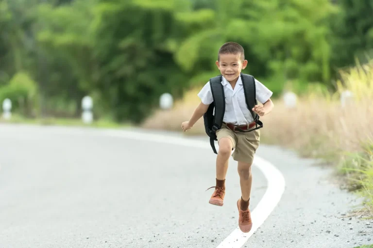 A happy young boy in school uniform running with his school bag